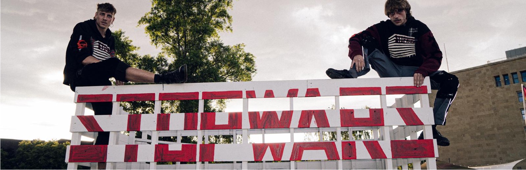 The two founders of WaMü Kollektiv sitting above a handmade WaMü artwork